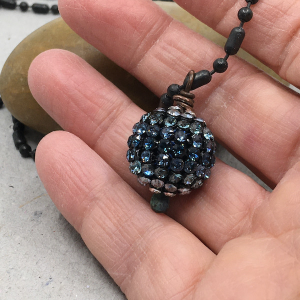 Hand holding a large ombre blue round crystal bead on black chain.