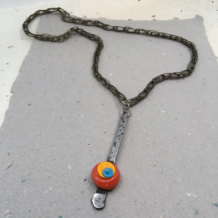 Necklace of woven dark silver metal chain with orange, gold and blue lampwork on long silver metal piece.