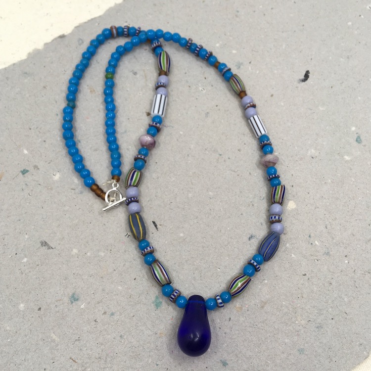 Necklace with large blue glass drop with various irregular striped tube beads and mostly blue or purple round glass beads. 