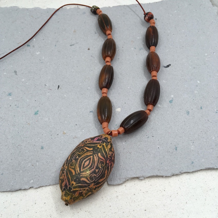Necklace with large pod pendant with a intricate pattern in black, orange and pink and light orange glass beads and large horn beads on leather.