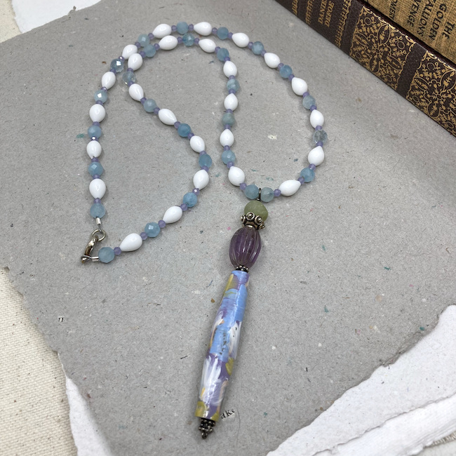 Necklace with long floral bead and white, purple and blue beads. 