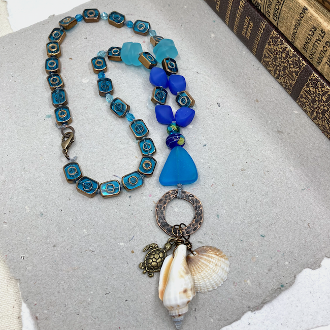 Necklace with various blue beads and a pendant with shell charms and a metal turtle. 